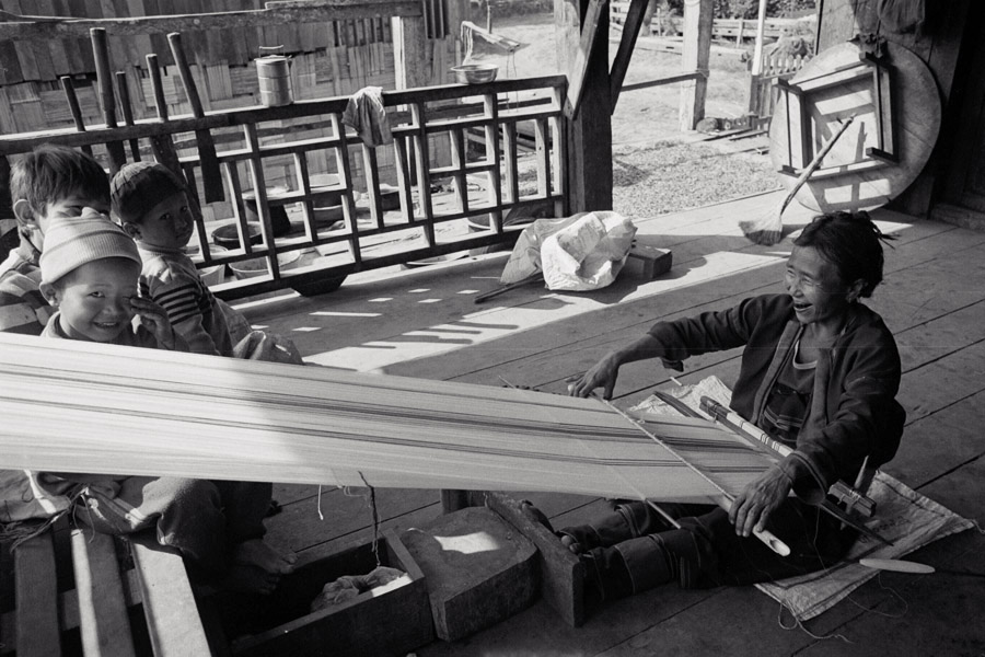 Pan Ta Pay, Northern Shan State 2011: Palaung woman weaving fabric for a new bag while neighbor kids keep her company. The 43-year-old emigrated from China as a child and met her husband in Myanmar (also a Palaung from China). She is wearing the traditional waist/hip rings of the Palaung costume.

<br><br>Every few years, she makes a new bag in white fabric with pink stripes. It takes about one month to finish on a backstrap loom.
